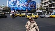 A woman walks past a billboard depicting a Persian legendary hero and flying figure hitting U.S. aircraft carriers alongside the message in English and Farsi: "From the Persia