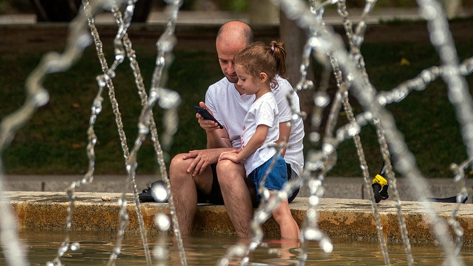 رجل وطفلة يتبردان عند نافورة في حديقة خلال موجة حر في مدريد، يوم 14 آب/أغسطس 2021.