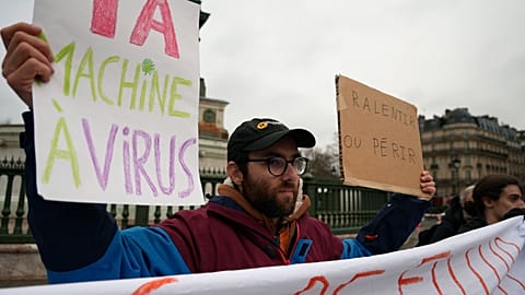 Demonstrators hold up banners and during a protest on Paris' Bastille Square, Monday, Feb. 10, 2025. Signs in French read "slow down or perish" and "AI virus machine". 