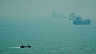 A motorboat travels past commercial vessels anchored amid haze in the Strait of Hormuz off Bandar Abbas, Iran, Monday, Sept. 7, 2026.