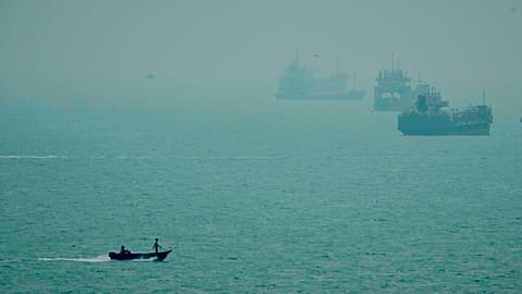 A motorboat travels past commercial vessels anchored amid haze in the Strait of Hormuz off Bandar Abbas, Iran, Monday, Sept. 7, 2026.