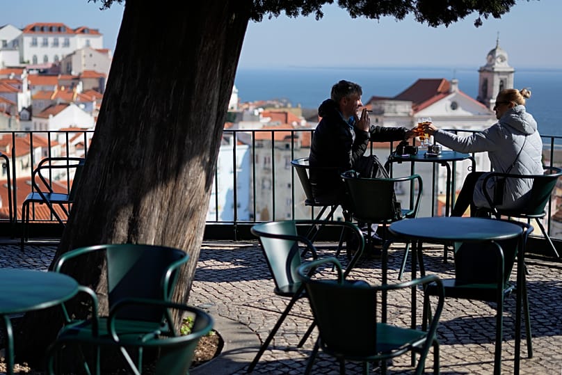 A couple clink beer glasses on the terrace of a kiosk overlooking Lisbon's historic Alfama neighbourhood