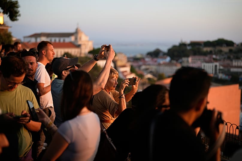 Tourists photograph the sunset from the Nossa Senhora do Monte viewpoint, looking out over central Lisbon and the River Tagus