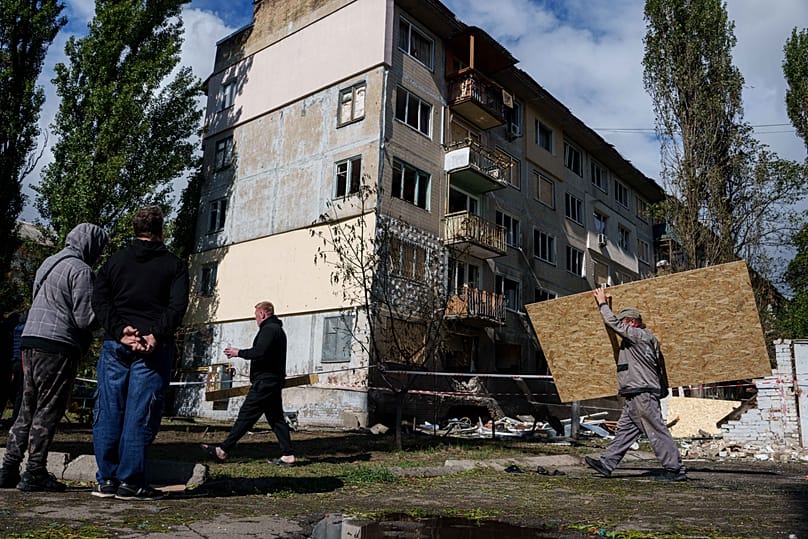 A municipal worker carries plywood to board up windows of an apartment building damaged by a Russian drone strike in Kyiv, 22 September, 2026