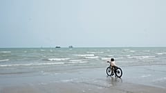 Un niño se detiene con su bicicleta en la orilla de la playa, mirando barcos comerciales anclados en el estrecho de Ormuz junto a Bandar Abbas, siete de septiembre de 2026