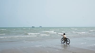 Rapaz para com a bicicleta à beira-mar, olhando para navios comerciais ancorados no estreito de Hormuz, ao largo de Bandar Abbas, 7 setembro 2026