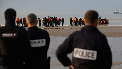Französische Polizisten beobachten in Gravelines, wie Migranten nach einem gescheiterten Versuch, nach Großbritannien überzusetzen, an den Strand zurückkehren, 6. November 2025