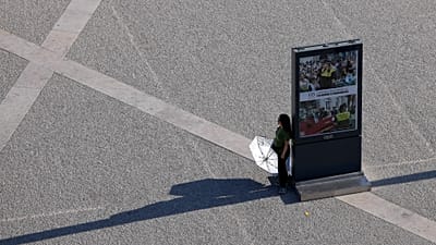 Una persona sostiene un paraguas y se detiene a la sombra de un panel informativo mientras cruza la plaza del Comercio, en Lisboa, en un caluroso día de septiembre