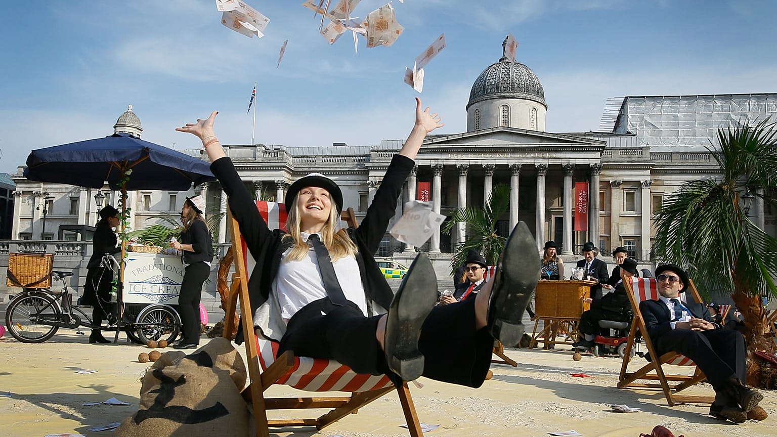 A protestor throws fake money into the air as she relaxes on a deckchair in an interactive, tropical tax haven beach in Trafalgar Square in London, Thursday, May 12, 2016.