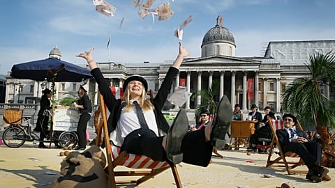 A protestor throws fake money into the air as she relaxes on a deckchair in an interactive, tropical tax haven beach in Trafalgar Square in London, Thursday, May 12, 2016.