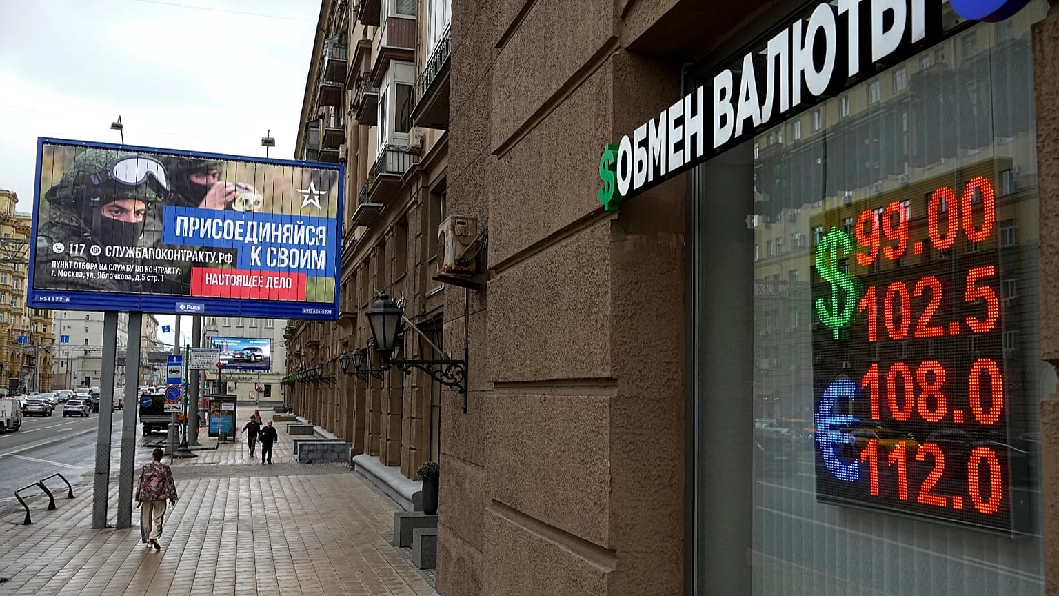 People walk past a currency exchange office with an army recruiting billboard calling for a contract for service in the Russian armed forces in Moscow, 14 August, 2023
