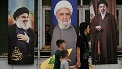 امرأة وأطفالها يحملون رايات "حزب الله" أثناء مرورهم أمام ملصقات تحمل صور كل من الأمين العام الراحل للحزب حسن نصر الله (يساراً)، والقيادي في الحزب نعيم قاسم (وسطاً)، والمرشد ال