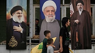 امرأة وأطفالها يحملون رايات "حزب الله" أثناء مرورهم أمام ملصقات تحمل صور كل من الأمين العام الراحل للحزب حسن نصر الله (يساراً)، والقيادي في الحزب نعيم قاسم (وسطاً)، والمرشد ال