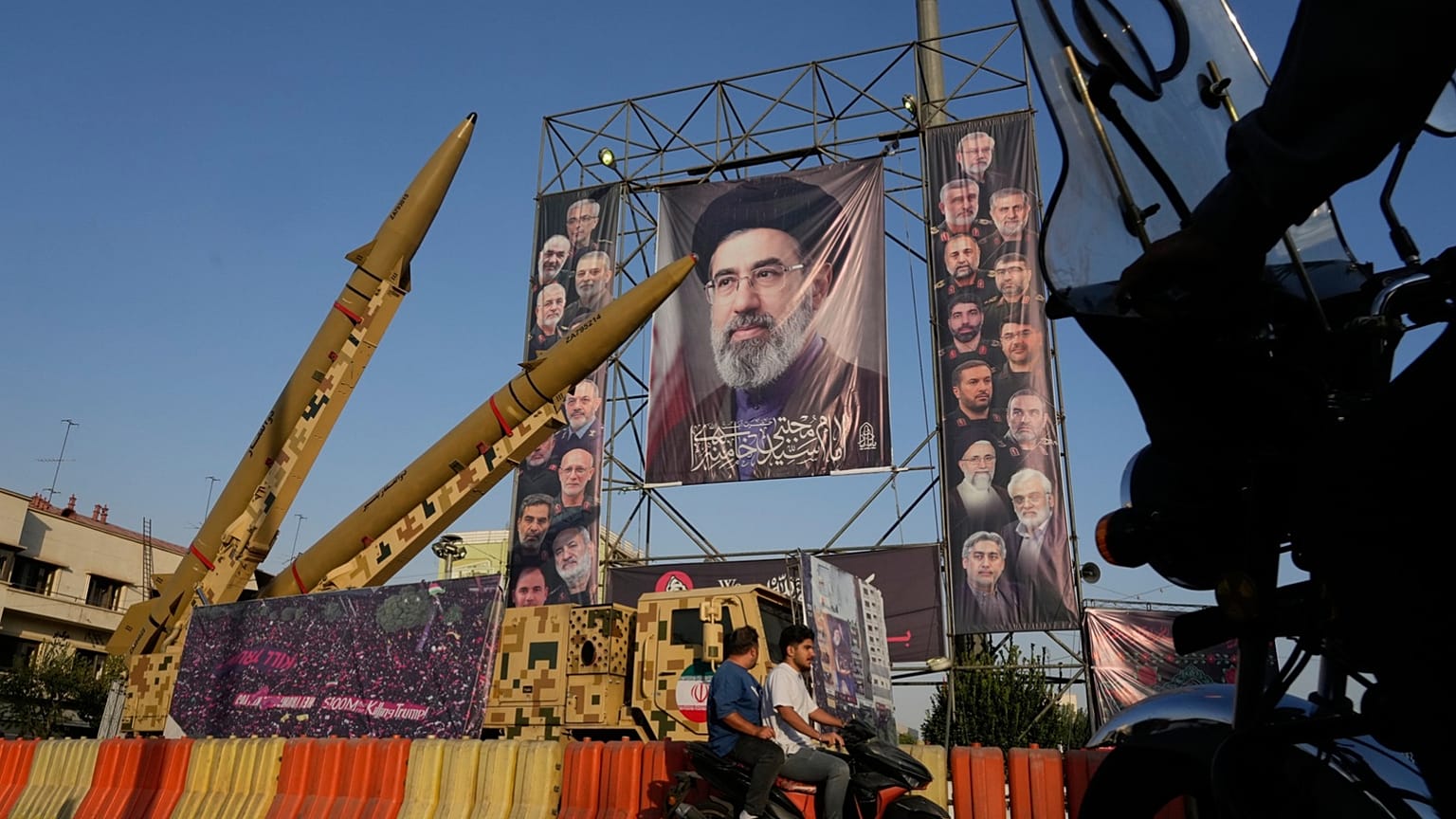موتورسواران در کنار موشک‌های ایرانی و تصاویر رهبر ایران و فرماندهان و دانشمندان کشته‌شده در حملات اسرائیل و آمریکا، در جریان یک نمایشگاه نظامی در میدان بهارستان تهران.