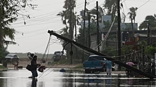 Un hombre transporta objetos a través de aguas inundadas, pasando junto a líneas eléctricas derribadas tras el paso de Polo, el 29 de septiembre de 2026. 