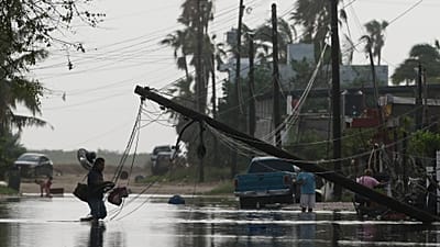 Un hombre transporta objetos a través de aguas inundadas, pasando junto a líneas eléctricas derribadas tras el paso de Polo, el 29 de septiembre de 2026. 