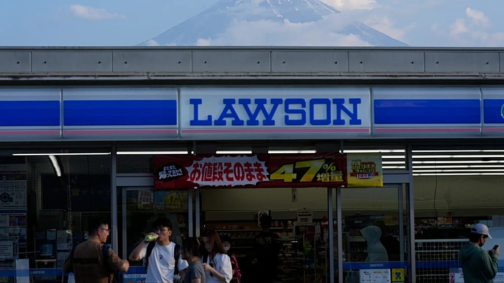 People shop at a convenience store as Mount Fuji is seen behind the store in Fujikawaguchiko town, about 110 kilometers (68 miles) west of Tokyo, Friday, June 14, 2024.