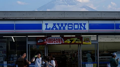 People shop at a convenience store as Mount Fuji is seen behind the store in Fujikawaguchiko town, about 110 kilometers (68 miles) west of Tokyo, Friday, June 14, 2024.