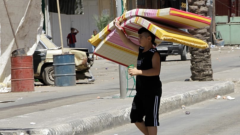 طفل يحمل فُرُشاً يعبر "شارع سوريا" الفاصل بين باب التبانة وجبل محسن بطرابلس اللبنانية وسط اشتباكات دامية، 23 آب 2012.