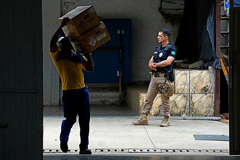 Um trabalhador transporta caixas com máquinas de votação eletrónica para o interior de uma escola pública, enquanto um agente de segurança permanece nas proximidades