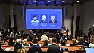Portraits of Karl Deisseroth, Peter Hegemann and Georg Nagel are shown on the screen as they are awarded the 2026 Nobel Prize in Physiology or Medicine.