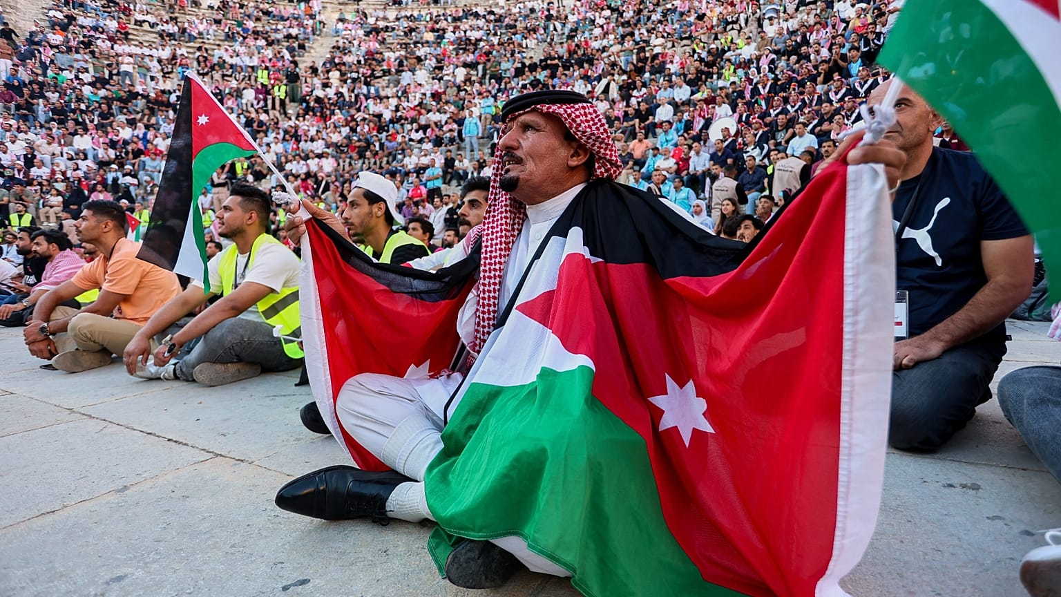 مشجع أردني بالكوفية والأعلام يتابع مباراة الأردن والأرجنتين بكأس العالم عبر شاشة عملاقة بالمدرج الروماني وسط عمّان، فجر الأحد 28 يونيو