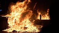 Un manifestante passa accanto a cassonetti dei rifiuti in fiamme dopo una protesta sulla crisi abitativa in Spagna, a Barcellona, il 5 ottobre 2026.