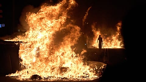 Ένας διαδηλωτής περνά δίπλα από φλεγόμενους κάδους σκουπιδιών μετά από πορεία για την κρίση στέγης στην Ισπανία, στη Βαρκελώνη, στις 5 Οκτωβρίου 2026.