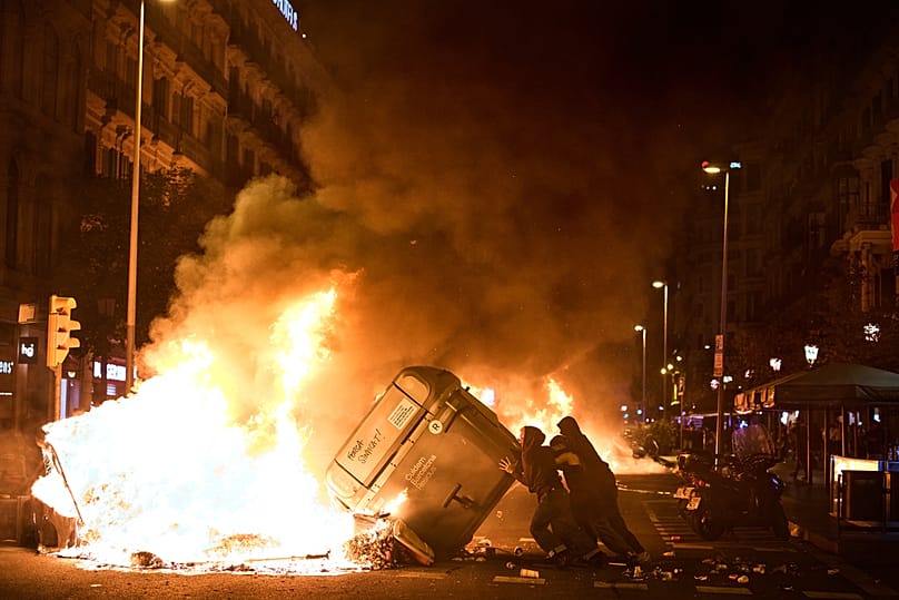 Protesters set trash cans on fire during clashes with police in a protest over Spain's housing crisis hours after Sánchez announced a snap election, in Barcelona, Oct. 5, 2026