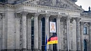 Ein Gedenkband mit der Aufschrift "7. Oktober 2023" hinter den auf Halbmast gehissten Flaggen, 7. Oktober 2024, Berlin