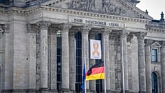 Ein Gedenkband mit der Aufschrift "7. Oktober 2023" hinter den auf Halbmast gehissten Flaggen, 7. Oktober 2024, Berlin
