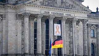 Ein Gedenkband mit der Aufschrift "7. Oktober 2023" hinter den auf Halbmast gehissten Flaggen, 7. Oktober 2024, Berlin