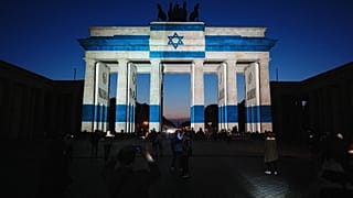 Participants stand in front of the Brandenburg Gate, illuminated by the Israeli flag, and pay tribute to the victims of the Oct. 7 Hamas lead attack on Israel,