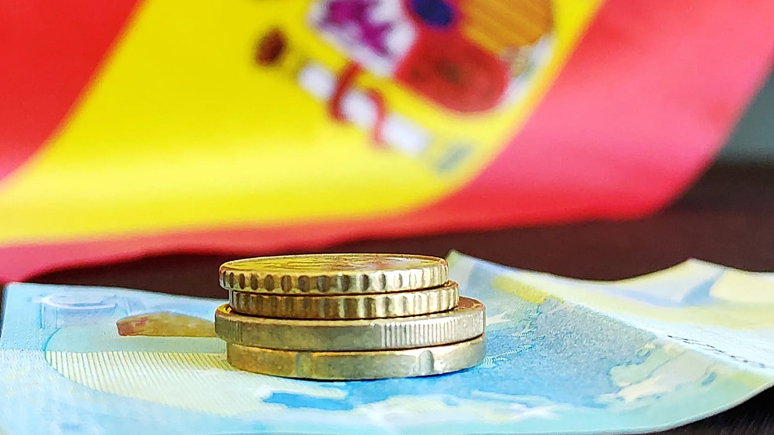 Un par de monedas y un billete con la bandera de España de fondo