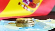 Un par de monedas y un billete con la bandera de España de fondo
