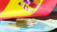 Un par de monedas y un billete con la bandera de España de fondo