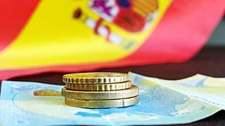 Un par de monedas y un billete con la bandera de España de fondo