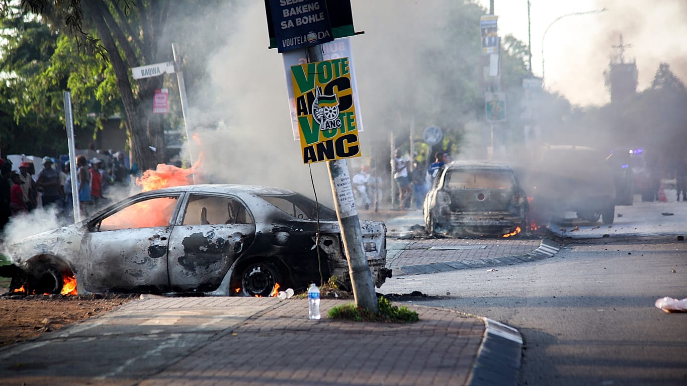 A car burns near a political party poster after it was set alight during protests related to immigration issues in Soweto.