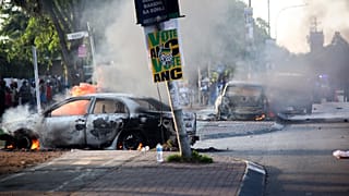 Egy autó ég egy párt plakátja mellett, miután felgyújtották a Sowetóban a bevándorlással kapcsolatos tüntetések során.