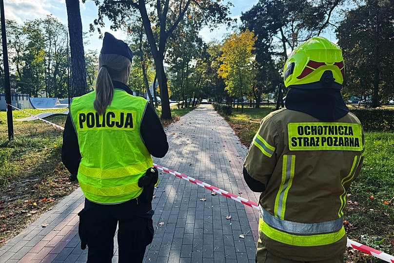 Policjantka i strażak ochotnik spoglądają wzdłuż ulicy w pobliżu odgrodzonego terenu po ataku na Zespół Szkół Zawodowych nr 4 w Ostrołęce, w środę, 7 października 2026 r.