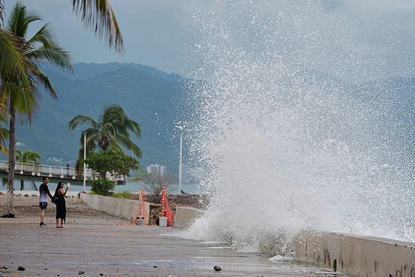 Unos turistas fotografían cómo el agua salpica contra la pared a medida que el huracán Simón se acerca a Puerto Vallarta, México, el domingo 11 de octubre de 2026.