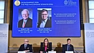 Portraits of Robert Hall and Michael Woodford on a screen at the Royal Swedish Academy of Sciences in Stockholm, 12 October, 2026