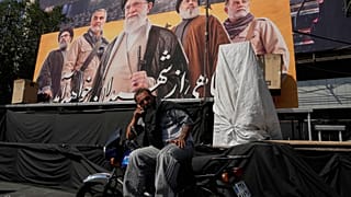 رجل يتحدث عبر الهاتف أمام لوحة تضم صور المرشد الإيراني السابق علي خامنئي وقادة إيرانيين ولبنانيين سابقين، في ساحة الثورة بالعاصمة طهران، 12 أكتوبر 2026. (أ ب)