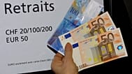 Eine Frau hält 100 Euro in rosa Scheinen unten und 100 Schweizer Franken in einer blauen Note oben, abgehoben an einem Bankautomaten in Genf am Dienstag, 8. Januar.
