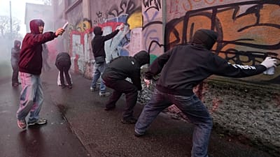 Protesters spray paint on a wall during a demonstration against ICE organized by students at the 2026 Winter Olympics, in Milan, Italy, Friday, Feb. 6, 2026