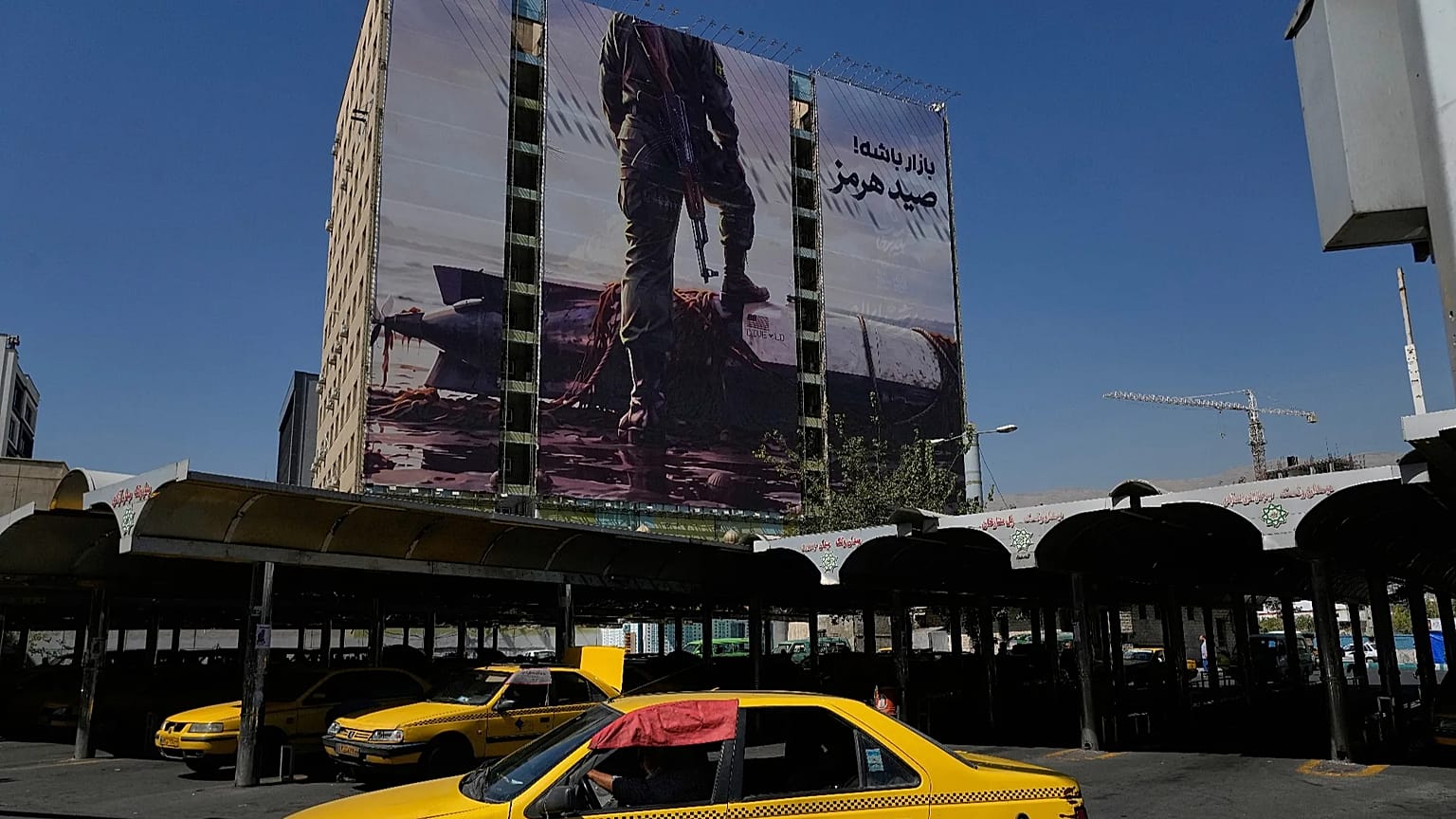 تمر سيارة أجرة بجوار لوحة إعلانية في أحد ميادين شمال طهران، يوم الأربعاء 23 سبتمبر 2026، تظهر عنصراً من الحرس الثوري الإيراني يضع قدمه على مركبة أمريكية مسيرة تحت الماء