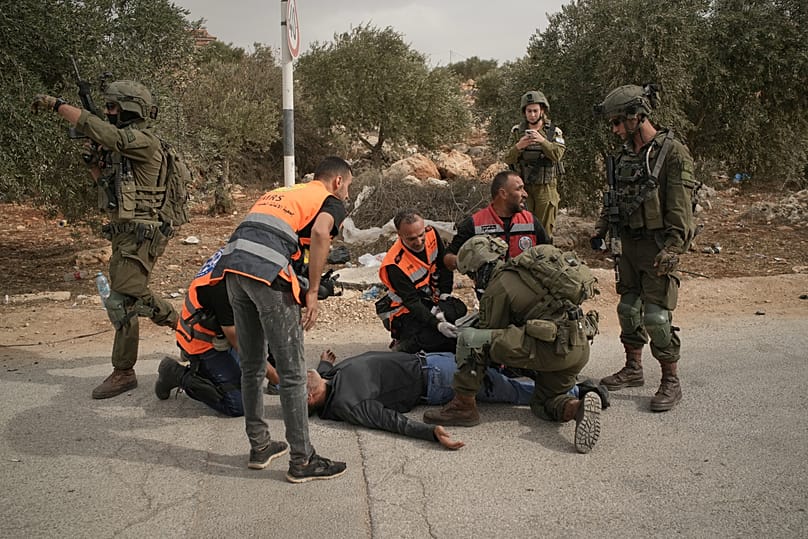 مسعفون فلسطينيون وجندي إسرائيلي يسعفون فلسطينياً أصيب برصاص الجيش عقب اعتداء مستوطنين على قاطفي الزيتون بالضفة الغربية، 16 أكتوبر 2026.