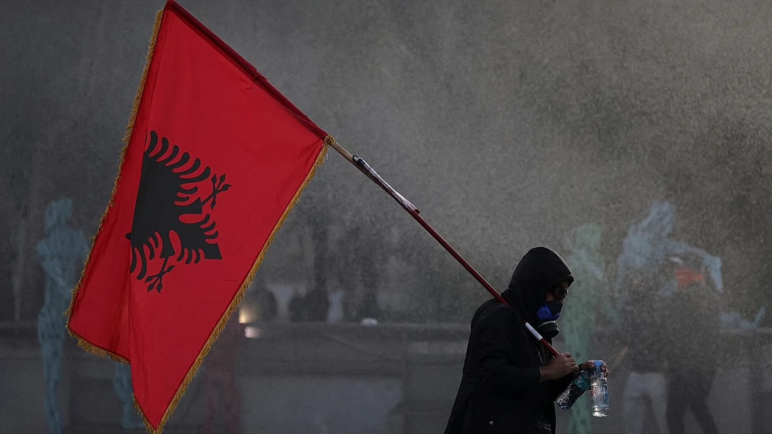  A hooded protester holding an Albanian flag is sprayed by a police water cannon during an anti-government protest in Tirana, 16 October 2026.
