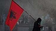  A hooded protester holding an Albanian flag is sprayed by a police water cannon during an anti-government protest in Tirana, 16 October 2026.