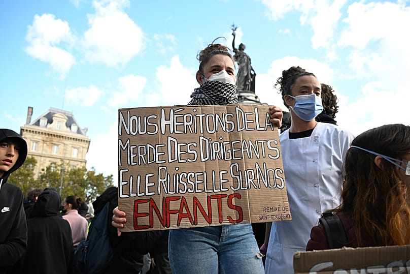 A protesters holds a placard reading "We inherit the crap of our leaders, and it trickles down onto our children", Paris, Saturday, Oct. 17, 2026